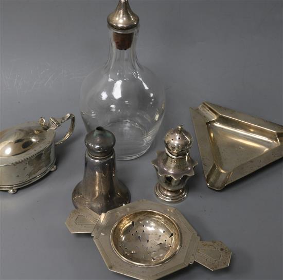 An Art Deco silver tea strainer, a silver ashtray, three silver condiments and a white metal mounted glass scent? bottle.